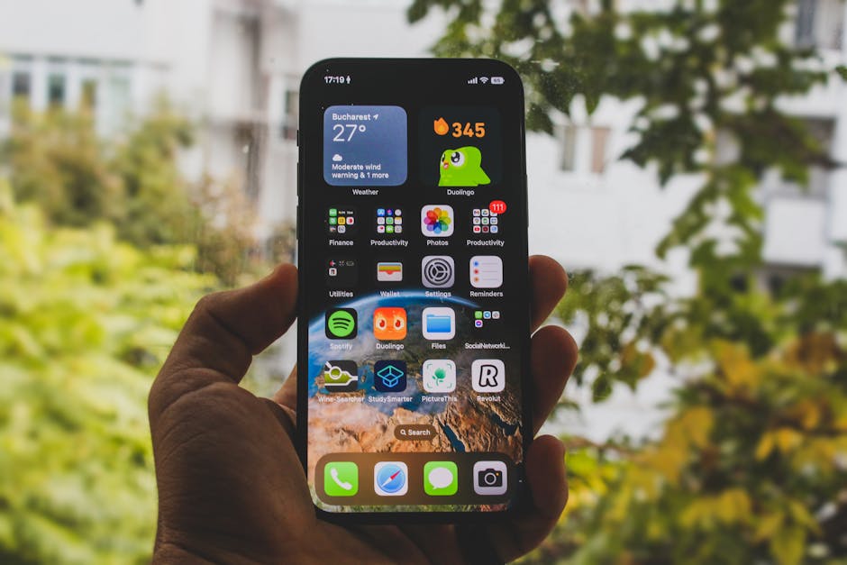 Close-up of a smartphone held outdoors in an autumn setting, showcasing apps and widgets.