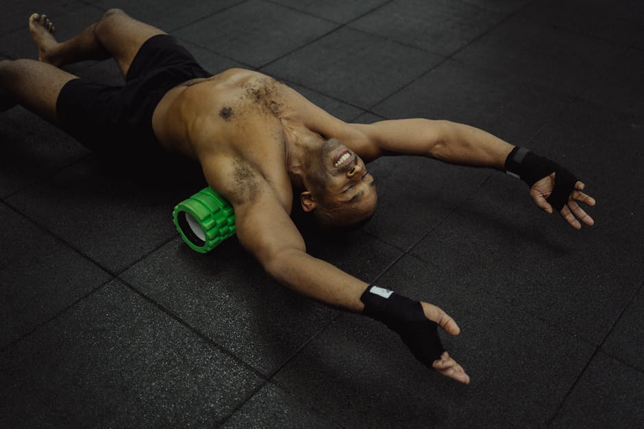 Shirtless man exercising with a foam roller in a fitness center.